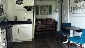 Ein kompakter Wohnraum mit Küchenzeile, einem Essbereich mit blauen Stühlen, einem braunen Sofa und einem Deckenventilator.