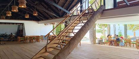 A wooden staircase with a natural design, leading to an outdoor area with wooden tables and chairs.