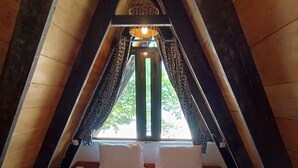 A cozy, triangular attic bedroom with a bed, pillows, and a window with curtains.