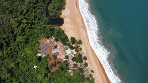 An aerial view of a beach resort with solar panels, a swimming pool, and dense greenery.