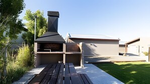 Una cocina exterior moderna con una parrilla, un banco de madera y un área empedrada.
