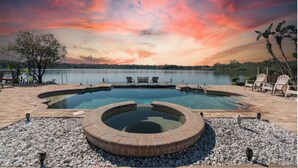 A swimming pool with a hot tub, surrounded by a deck with chairs and a view of a lake and sunset. - Luxury Hideaway - Lakefront - Mini Golf, Pool + More! (Seffner)