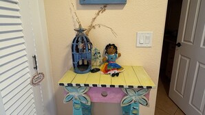 Un couloir orné d’une table décorative sur laquelle sont disposés un panneau évoquant des souvenirs de la mer, une petite figurine et une cage à oiseaux bleue.