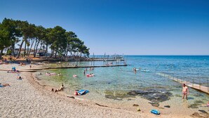 A beach with clear shallow waters, a pier, and people swimming and sunbathing.