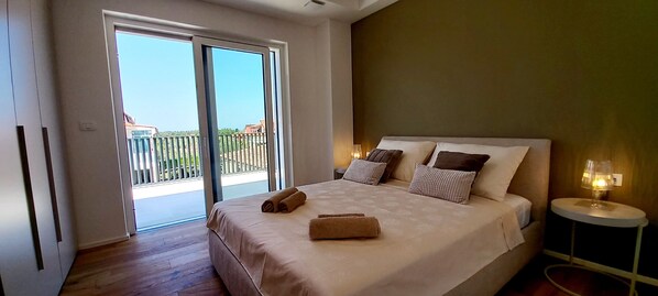 A bedroom with a large bed, a balcony, and a nightstand with a lamp.