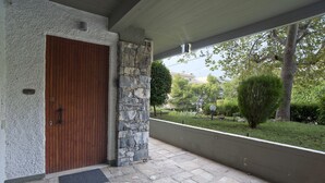 A stone exterior wall, a wooden door, and a view of a green landscape with trees and a building in the background.