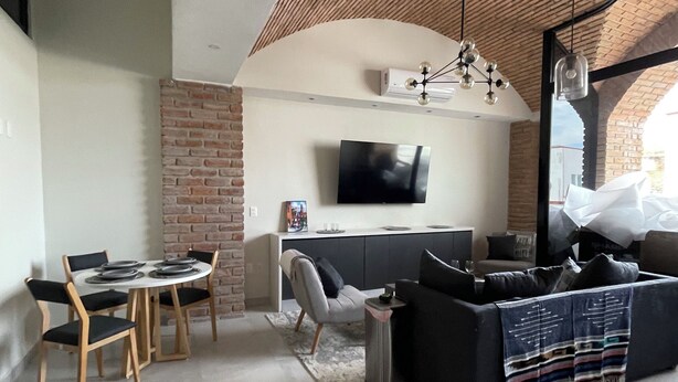 A modern living room with a dining area, a flat-screen TV mounted on the wall, and a large window providing natural light. - Bliss, in the heart of PV! 2-bedroom apartment with AC, WiFi in Puerto Vallarta (Puerto Vallarta)