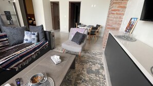 A modern living room with a grey sofa, a coffee table, and a dining area with a table and chairs. - Bliss, in the heart of PV! 2-bedroom apartment with AC, WiFi in Puerto Vallarta (Puerto Vallarta)