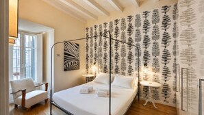 Un dormitorio con cama con dosel, una silla, una mesa redonda y una pared con diseño de árbol.