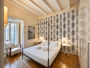 A bedroom with a four-poster bed, a chair, a round table, and a wall with a tree pattern. - Arche Verona Old Town Apartment (Verona)
