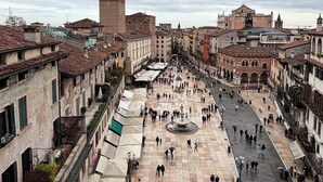Una plaza histórica con una imponente torre del reloj, rodeada de edificios tradicionales y una fuente en el centro.