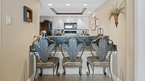 A kitchen with white cabinets, a granite countertop, and a central island with bar stools. - Upscale Oceanfront 3BR Condo • 14th Floor • Golf Course Views (Myrtle Beach)