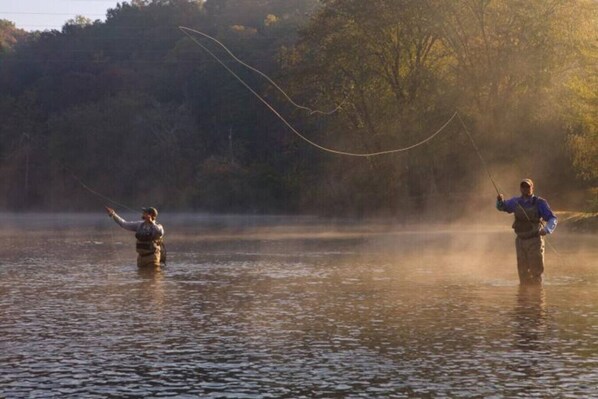 Two people fishing in a calm lake with trees in the background.