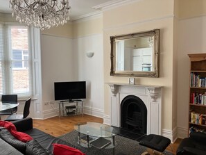 A living room with a fireplace, a television, a bookshelf, and a chandelier.