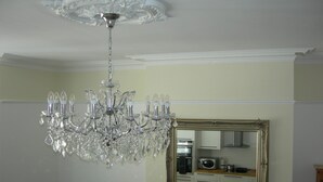 Un candelabro con múltiples brazos y detalles de cristal, un espejo grande y ornamentado, y una zona de cocina con electrodomésticos.
