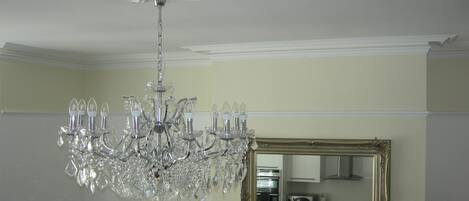 A chandelier with multiple arms and crystal decorations, a large ornate mirror, and a kitchen area with appliances.