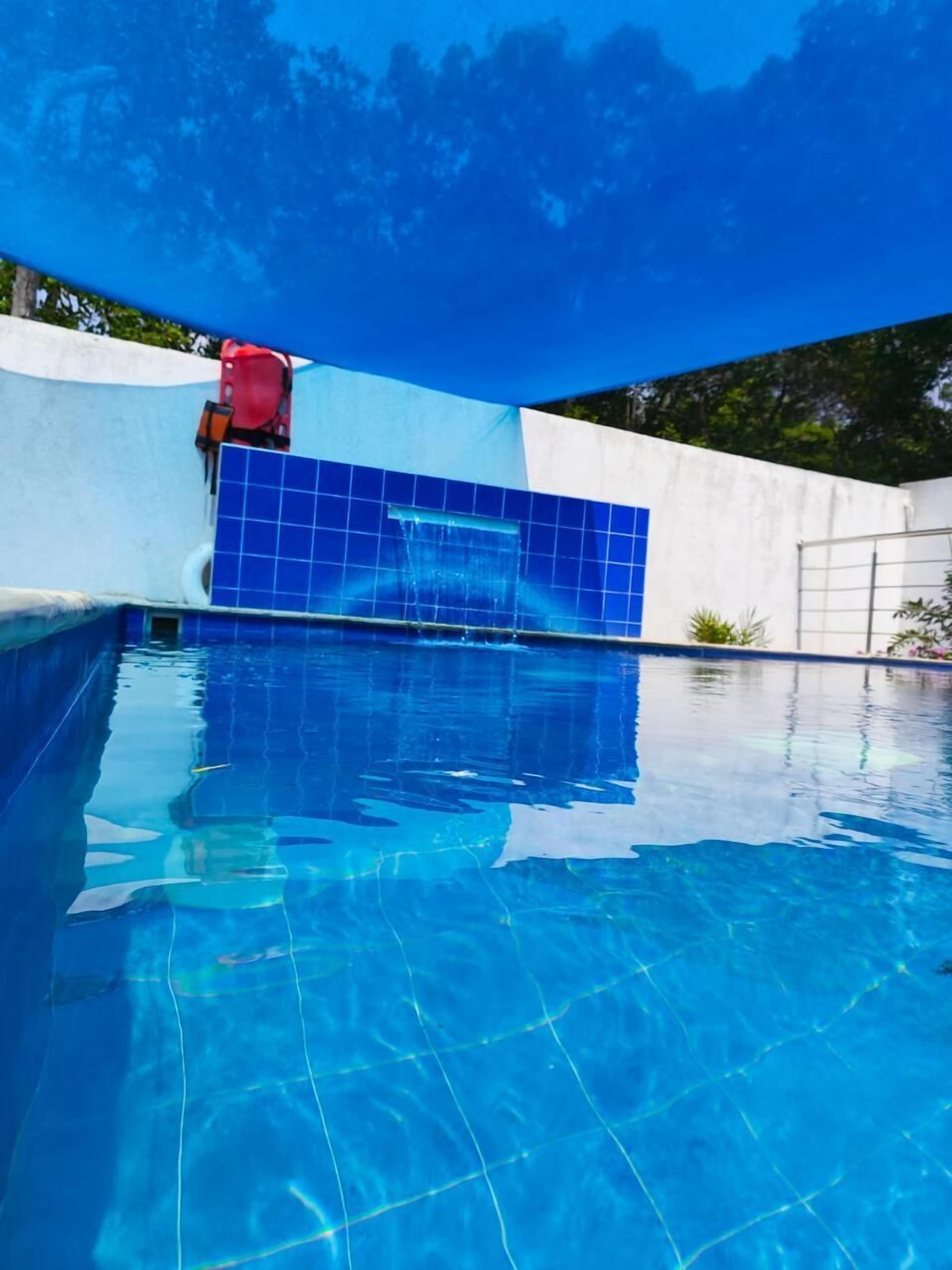 A clear blue swimming pool with a tiled wall and a red object on the left.