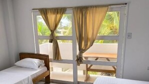 Une chambre avec deux lits simples, une tête de lit en bois et une grande fenêtre avec des rideaux.