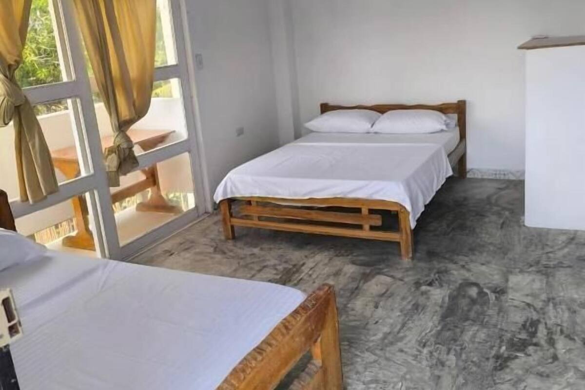 Una habitación con dos camas de madera, un ventanal con cortinas y suelo de mármol.