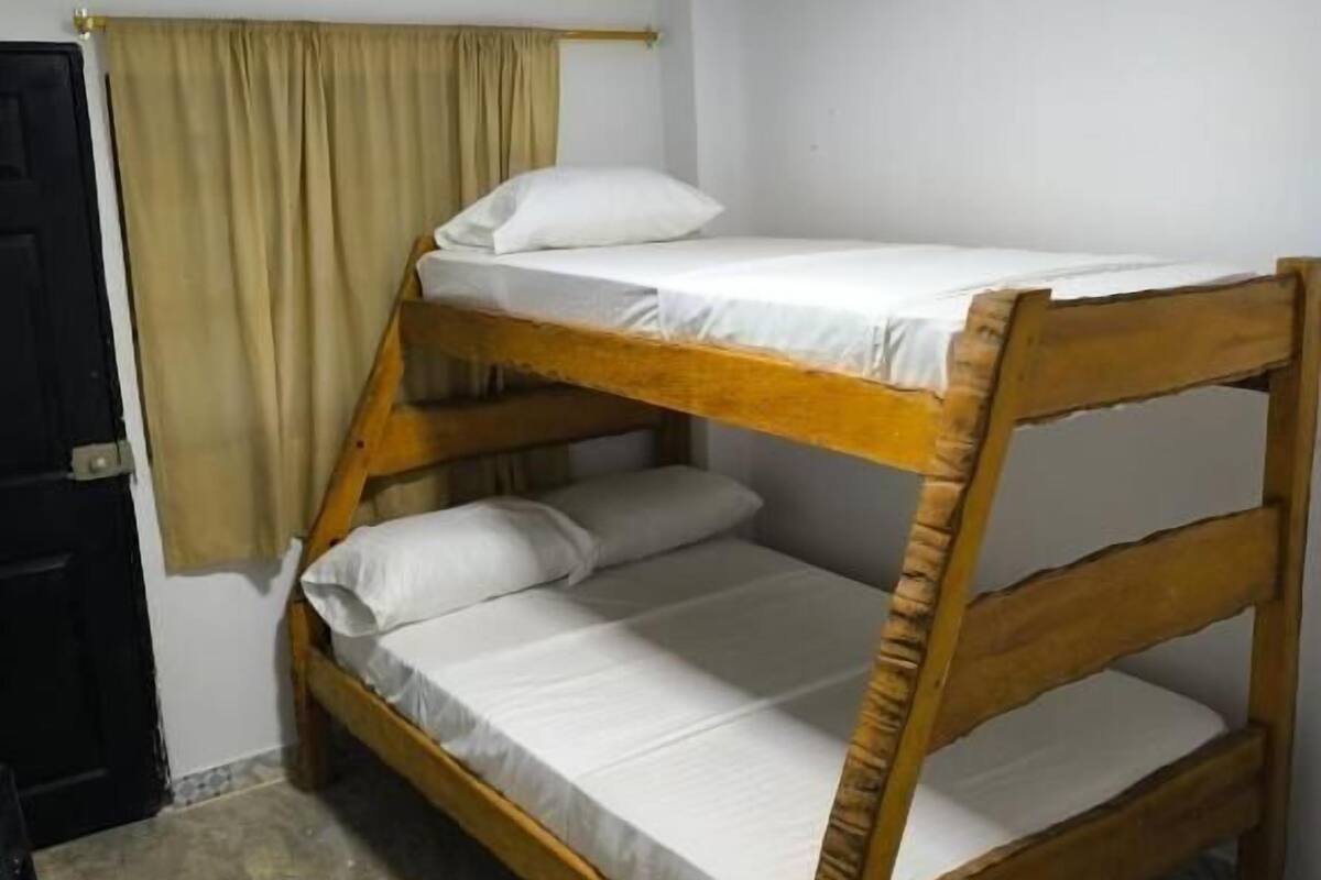 Habitación con literas, una lámpara en el techo, una puerta y una cortina.