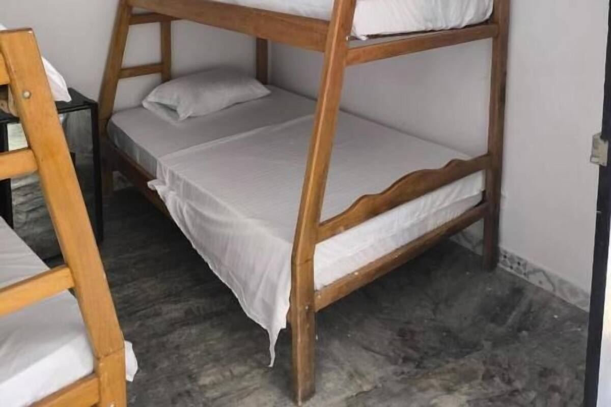 Dormitorio con literas, ropa de cama blanca y una escalera de madera.