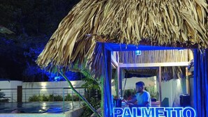 Une construction au toit de chaume, sur laquelle est accrochée une enseigne lumineuse au néon indiquant « PALMETTO ».