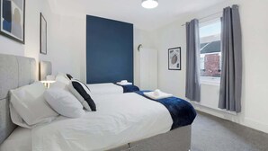 Habitación de hotel con cama, mesita de noche, lámpara, ventana con cortinas y vistas al exterior.