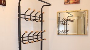 A black coat rack with multiple hooks against a white wall, a mirror reflecting the rack, and a painting above the mirror. - Acaccia Bunglow  (Carterton)