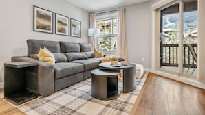 Ein modernes Wohnzimmer mit einem grauen Sofa, einem Couchtisch und einem großen Fenster mit Blick auf eine verschneite Landschaft.