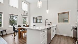 A modern kitchen with a central island, white cabinetry, and a dining area with a wooden table and chairs.