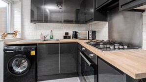A compact kitchen with a washing machine, a microwave, a stove, and black cabinets. - LFC Stay | 1 Min to Stadium | W/M | Pet Friendly (Anfield)