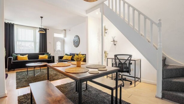 A modern living room with a sofa, coffee table, and a dining area with a table and chairs. A staircase is visible in the background. - LFC Stay | 1 Min to Stadium | W/M | Pet Friendly (Anfield)
