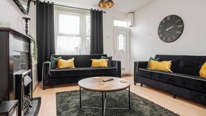A modern living room with two black sofas, a round coffee table, and a large wall clock. - LFC Stay | 1 Min to Stadium | W/M | Pet Friendly (Anfield)