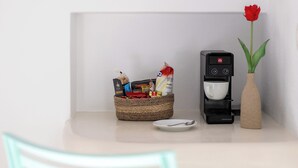 A coffee machine, a basket of snacks, a plate, and a vase with a red flower on a table.