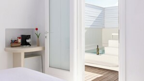 A modern bathroom with a glass door, a small bedside table with a coffee maker, a vase with a flower, and a view of a pool area.