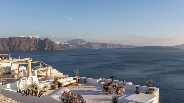 A rooftop terrace with a view of the sea and cliffs, featuring outdoor seating and potted plants. - Santorini Sun Villa Two in Oia | Private Hot Tub (Oia)