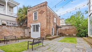 Une cour avec un bâtiment en briques, un sol pavé de pierres et deux bancs.