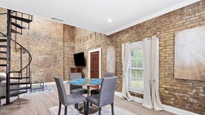 Un espace repas avec un mur en briques, un escalier en colimaçon, un téléviseur à écran plat et une grande fenêtre avec des rideaux.