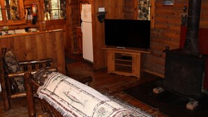A cozy cabin interior with a wooden interior, a television on a stand, a fireplace, and a bed with a patterned blanket. - Cozy Log Cabin in Cook Forest ~ Dog Friendly (Clarington)