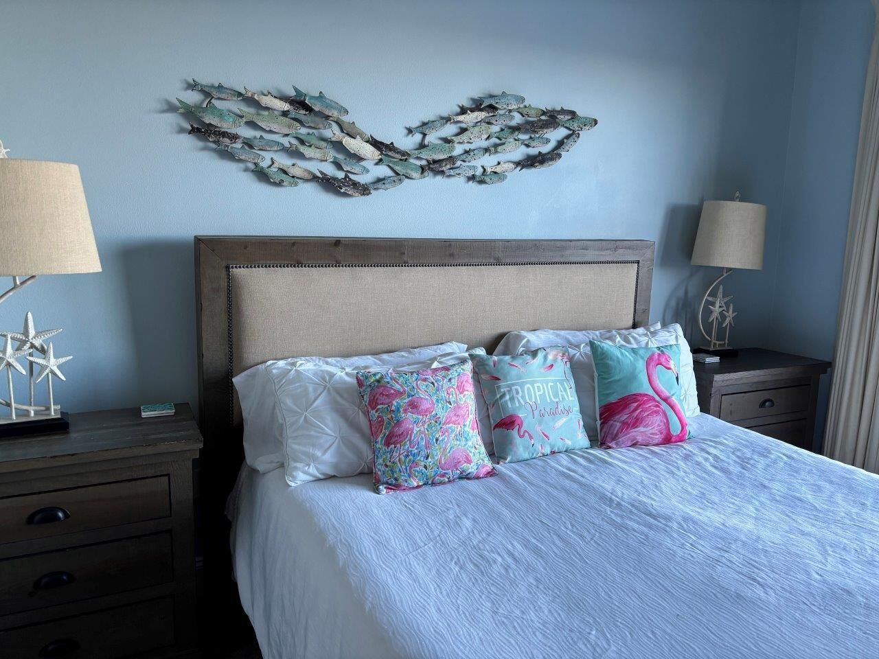 Una cama con edredón blanco, cabecera de madera y almohadas decorativas.