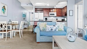 A cozy living room with a blue sofa, a dining area with white chairs, and a kitchen with wooden cabinets and a microwave. - Ease, Comfort and Tranquility at Lake Town Wharf Resort, Panama City Beach, FL (Panama City Beach)