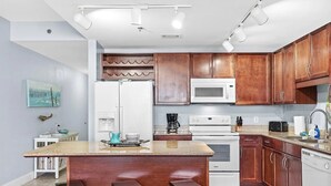 A modern kitchen with wooden cabinets, white appliances, and a central island with stools. - Ease, Comfort and Tranquility at Lake Town Wharf Resort, Panama City Beach, FL (Panama City Beach)
