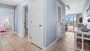 A spacious living area with a large sliding door leading to a balcony, a dining area with a table and chairs, and a bedroom with a pink bed and nightstand. - Ease, Comfort and Tranquility at Lake Town Wharf Resort, Panama City Beach, FL (Panama City Beach)