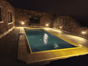Una piscina rettangolare circondata da un muro in pietra, illuminata da luci a parete.