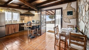 Une cuisine avec coin repas, des poutres en bois, un mur en pierre et une vue sur l’extérieur.