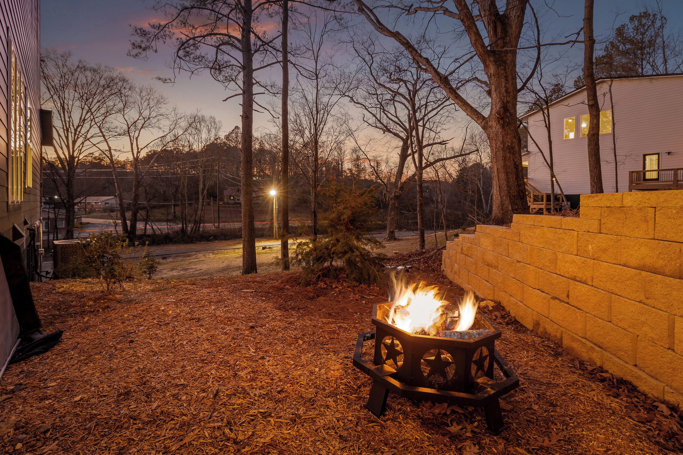 A backyard with a fire pit, a brick wall, and a house in the background.