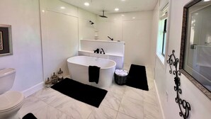 A modern bathroom with a freestanding bathtub, a toilet, and a vanity with a mirror. - Cora's Suite at the Flyin H Ranch (Tyler)