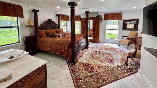 A spacious bedroom with a four-poster bed, a large window, and a view of the outdoors. - Cora's Suite at the Flyin H Ranch (Tyler)
