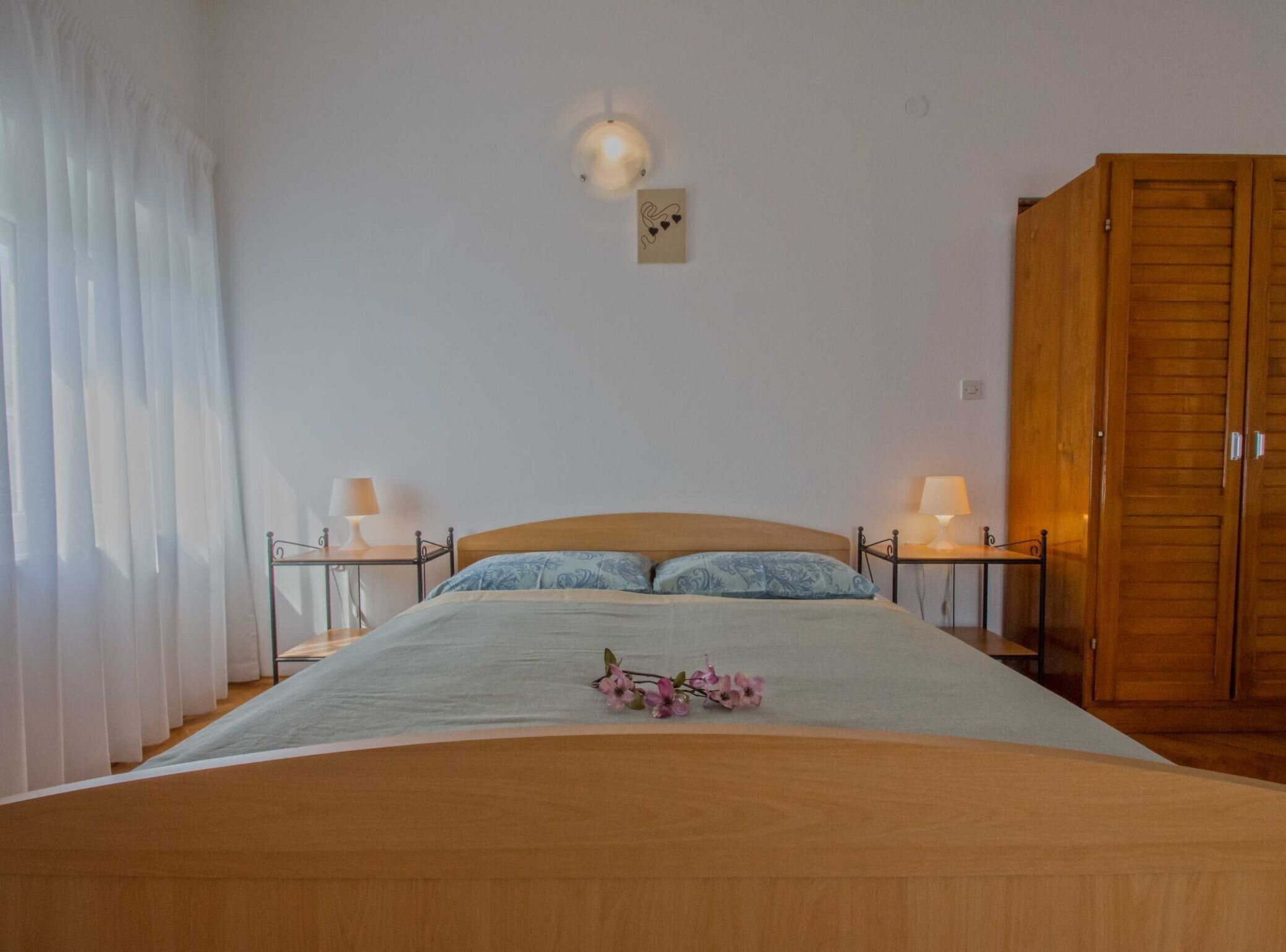 Quarto com cama, duas mesas de cabeceira com abajures, guarda-roupa de madeira e luminária na parede.