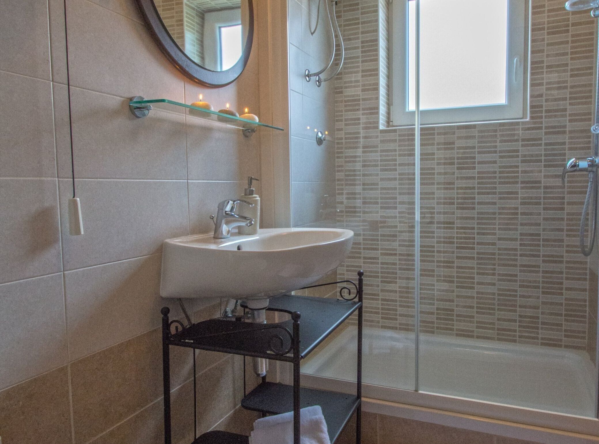 Een badkamer met een wastafel, spiegel, plank met kaarsen en een douche.